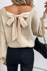 Back view of a woman wearing a cream knit sweater with a large bow detail on the back
