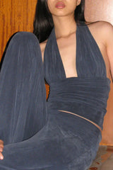 Close-up of a woman wearing a dark blue halter neck crop top and dark blue wide leg pants, seated.