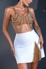 Close-up of a woman in a brown chain-and-bead embellished bralette top and a white high-slit skirt with fringe detailing.