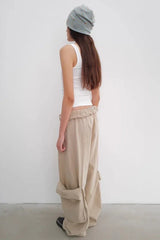 Rear view of a person wearing a white tank top and tan baggy cargo pants with prominent side pockets, and a striped beanie.