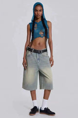 Woman wearing a blue distressed knit crop top with a hood and light wash wide-leg denim capri pants, a black belt, white socks, and black sneakers.