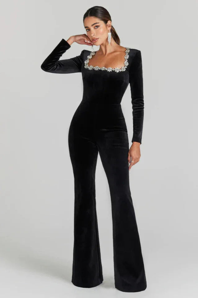 Full-length view of a woman in a black velvet jumpsuit with a rhinestone-embellished square neckline and flared legs.