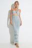 Woman wearing a light blue knit maxi dress with a halter neckline and cut-out detail, standing against a white backdrop.