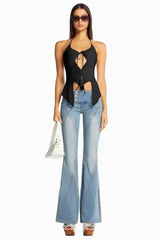 Woman wearing a black halter top with keyhole detail and tie closure, paired with light wash flared jeans with paneled design.