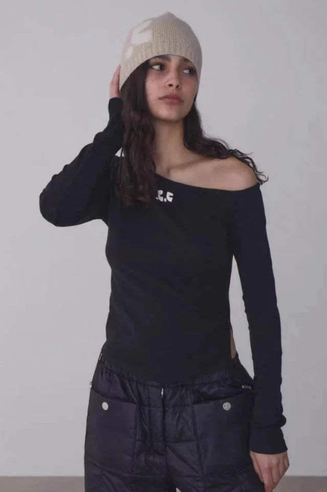 Woman wearing a black off-the-shoulder long-sleeve top with a beige beanie and black quilted pants, front view.