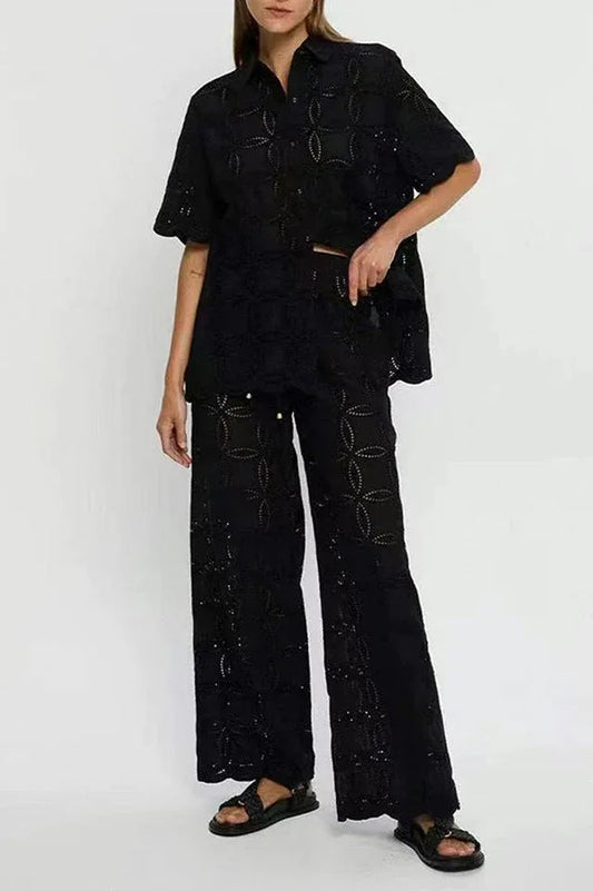 Woman wearing a black embroidered short-sleeve button-down shirt and wide-leg pants