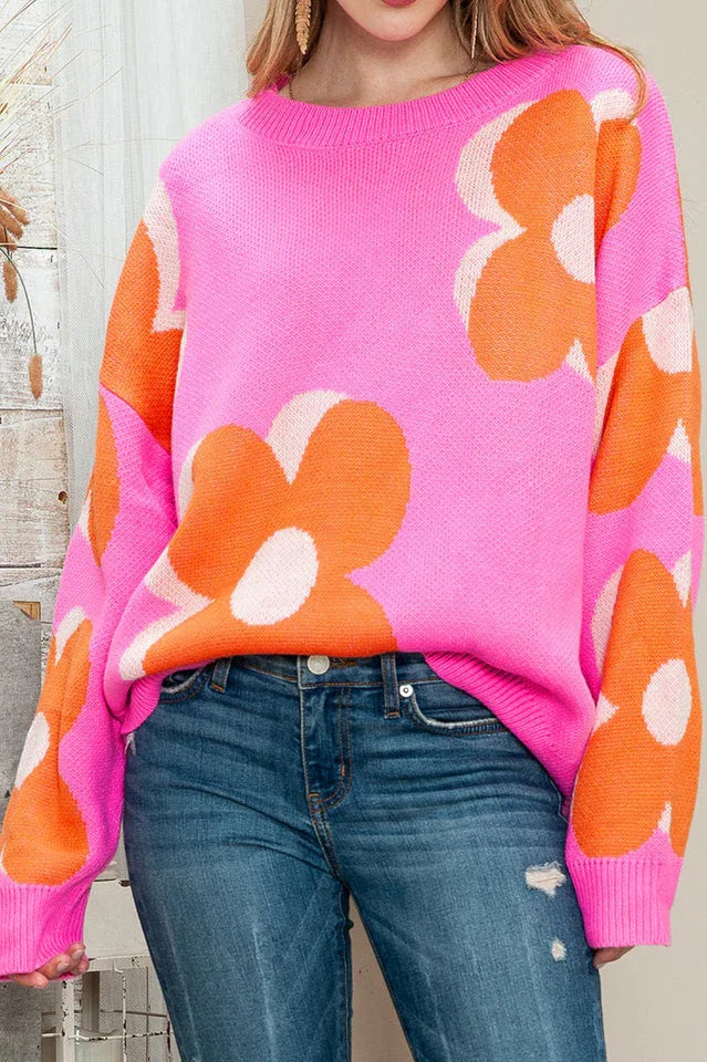 Close-up of the front of a pink crew neck sweater with an orange and white floral print.