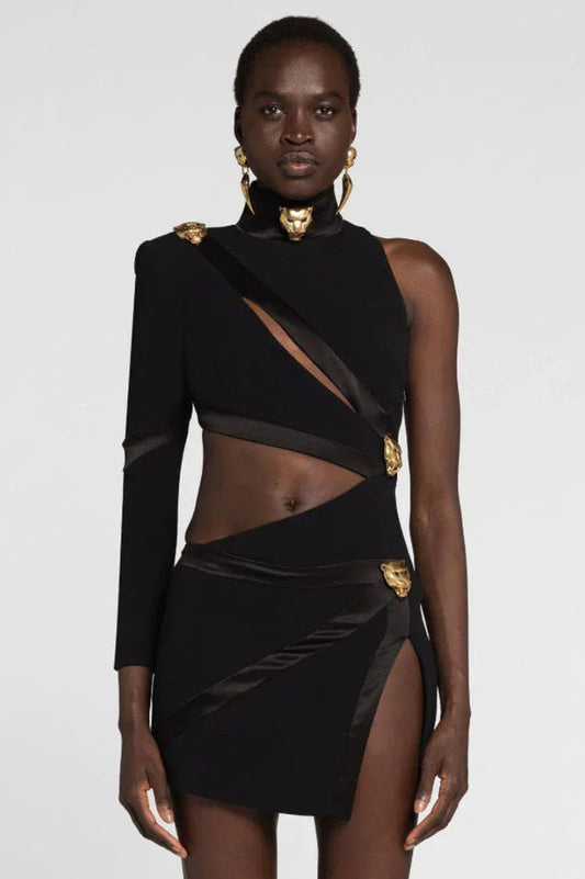 Model wearing a black asymmetrical one-shoulder mini dress with cut-out details and gold lion head embellishments.