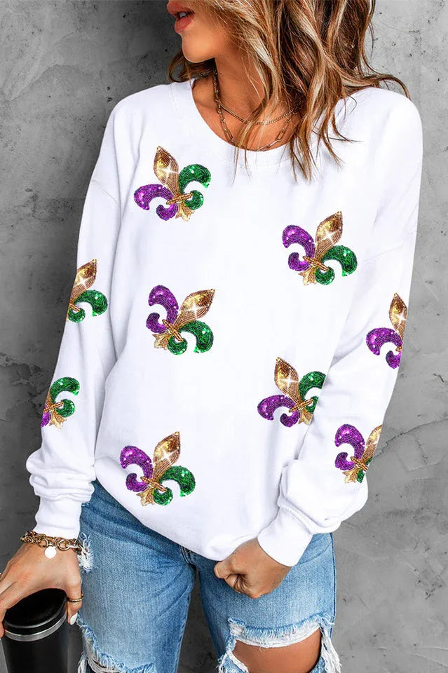 Close-up of a woman's torso wearing a white long-sleeved sweatshirt adorned with colorful sequin fleur-de-lis designs.