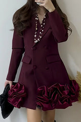 Woman wearing a maroon double-breasted blazer dress with a ruffled hem and holding a black clutch