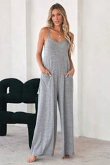 Woman wearing a grey wide leg jumpsuit with spaghetti straps and pockets, standing indoors.