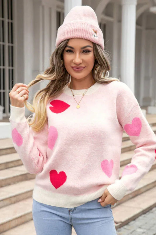 A woman wearing a pink heart print sweater and a pink beanie, holding her hair.