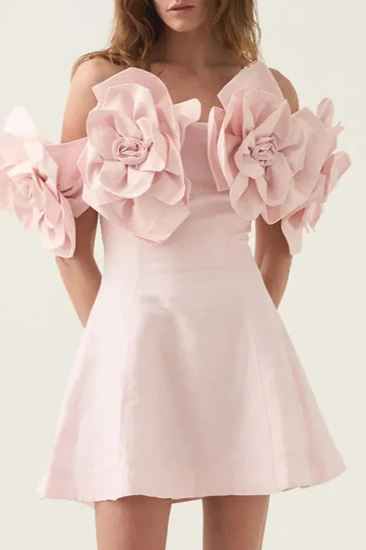 Model wearing a light pink off-the-shoulder mini dress with large floral embellishments on the shoulders.