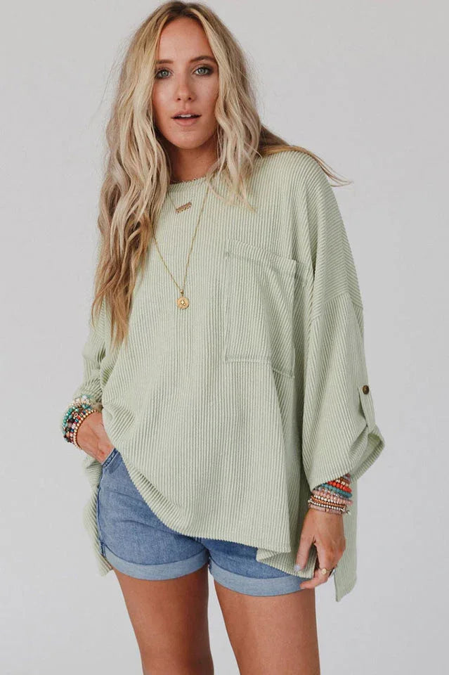 Woman wearing a light green ribbed long-sleeve top with a chest pocket and denim shorts.
