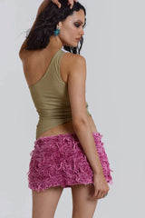 Back view of a woman in a one-shoulder sequined top and pink distressed denim shorts.