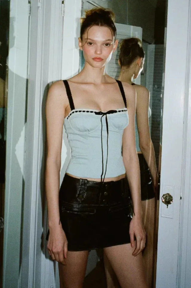 A young woman poses in a doorway wearing a light blue cropped top with black trim and a black mini skirt.