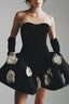 Woman wearing a black strapless cocktail dress with white floral appliqués and long black gloves