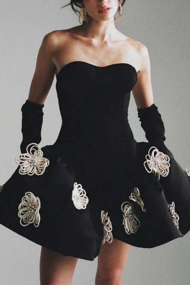Woman wearing a black strapless cocktail dress with white floral appliqués and long black gloves