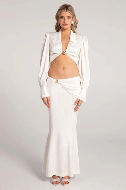 Woman wearing a white satin two-piece set consisting of a cropped long-sleeved top and a floor-length mermaid skirt.