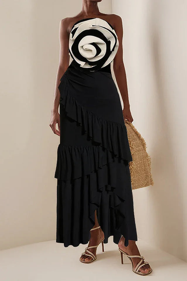 Woman wearing a black one-piece swimsuit with a black and white floral embellishment on the bust, paired with a black ruffled maxi skirt.