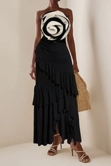 Woman wearing a black one-piece swimsuit with a black and white floral embellishment on the bust, paired with a black ruffled maxi skirt.