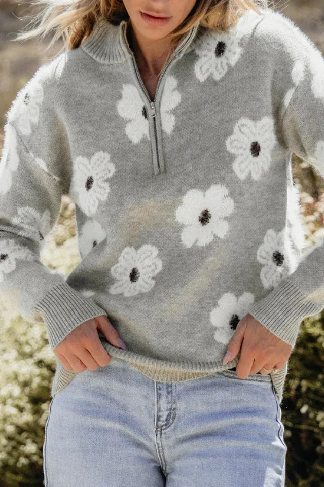 Close-up of a woman's torso wearing a gray floral print quarter-zip knit sweater and light wash denim jeans.