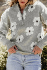 Close-up of a woman's torso wearing a gray floral print quarter-zip knit sweater and light wash denim jeans.