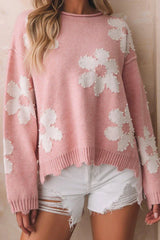 Close-up of a woman's torso wearing a pink knit sweater with a flower pattern and pearl embellishments.