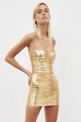 Woman wearing a gold metallic ruched mini dress with a sweetheart neckline and thin straps, hands on hips.