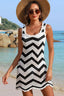 Woman wearing a black and white chevron crochet knit mini dress with a straw hat and sunglasses on a beach.