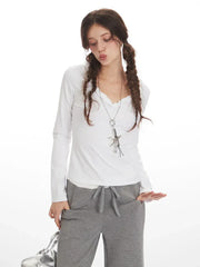 Close-up of a woman wearing a white long-sleeve shirt with ruffled neckline and grey sweatpants, with hands in pockets.