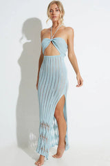 Woman wearing a light blue knit maxi dress with a halter neckline and cut-out detail, with a slit on the side.