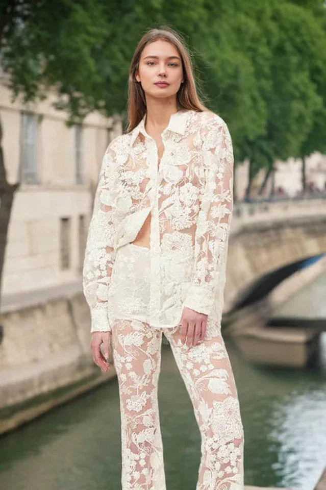 Woman wearing a sheer white lace button-down shirt and flare leg pants with a bridge and city skyline in the background.