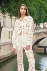Woman wearing a sheer white lace button-down shirt and flare leg pants with a bridge and city skyline in the background.