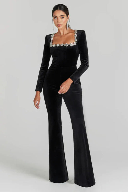 Woman wearing a black velvet jumpsuit with a square neckline and flared legs. The neckline is embellished with rhinestones.