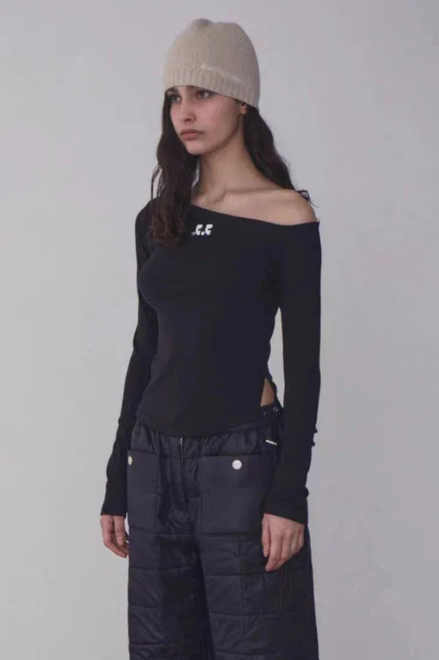 Woman wearing a black off-the-shoulder long-sleeve top with a beige beanie and black quilted pants, side view.