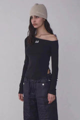 Woman wearing a black off-the-shoulder long-sleeve top with a beige beanie and black quilted pants, side view.