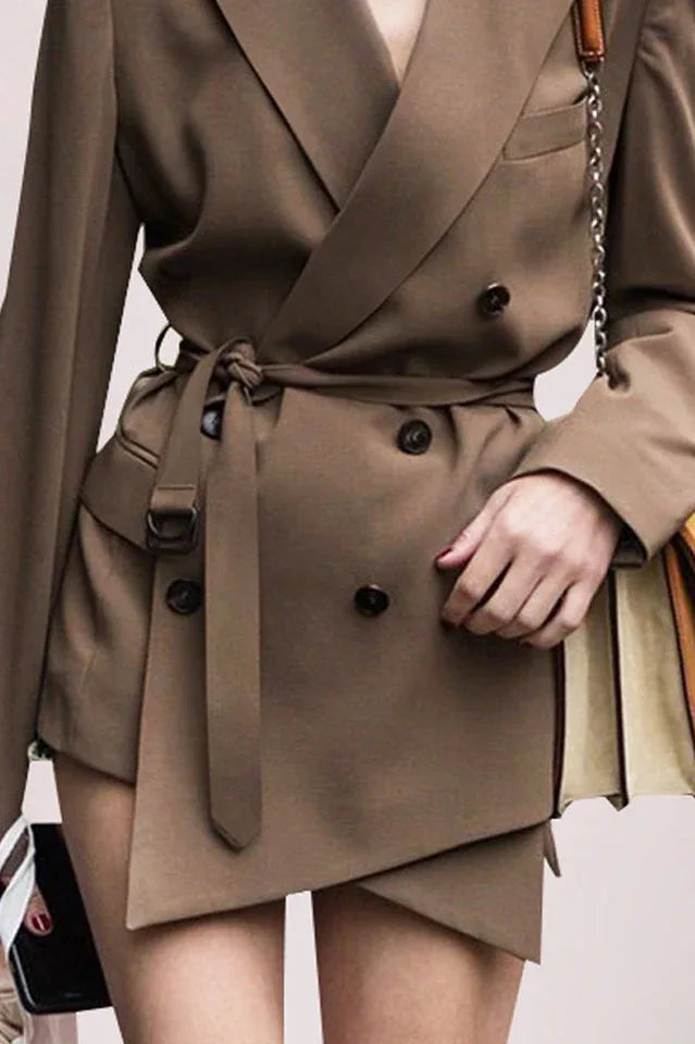 Close-up of the belted waist and asymmetrical hem of a brown double-breasted blazer.