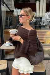 Close-up of a model wearing a white pleated mini skirt with a brown off-the-shoulder sweater.