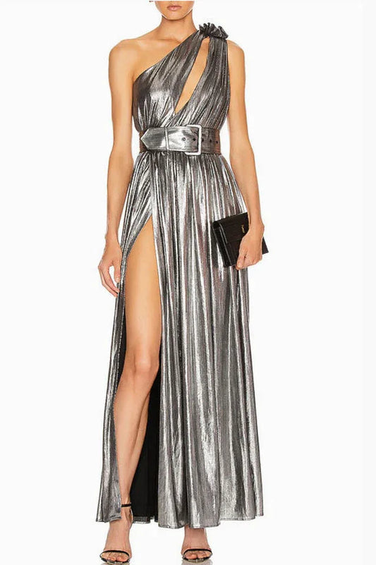 Model wearing a silver metallic one-shoulder gown with a high slit and a matching belt, holding a black clutch.