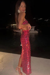 Woman wearing a pink sequined strapless top and matching full-length skirt posing on a balcony at night.