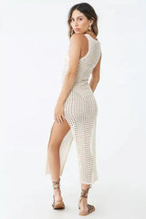 Back view of a woman wearing a cream crocheted knit sleeveless maxi dress with a high slit.
