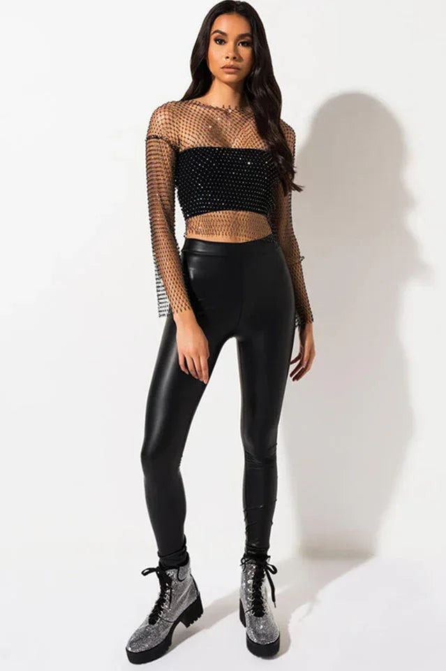 Full-body shot of a woman wearing the black sheer embellished crop top and black faux leather leggings.