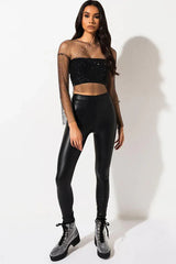Full-body shot of a woman wearing the black sheer embellished crop top and black faux leather leggings.