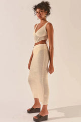 Woman wearing a cream crochet knit crop top and matching maxi skirt, side view.