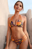 Woman in a colorful abstract print bikini with braided straps and cut-out bottoms, standing on stairs.