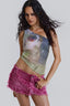 Woman wearing a one-shoulder sequined top with a graphic print and pink distressed denim shorts.