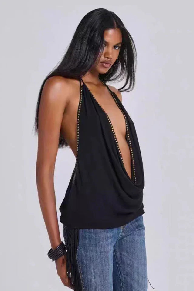 Model wearing a black halter top with a deep V-neck and studded trim, paired with blue jeans with fringe detailing.