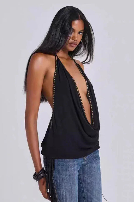 Model wearing a black halter top with a deep V-neck and studded trim, paired with blue jeans with fringe detailing.