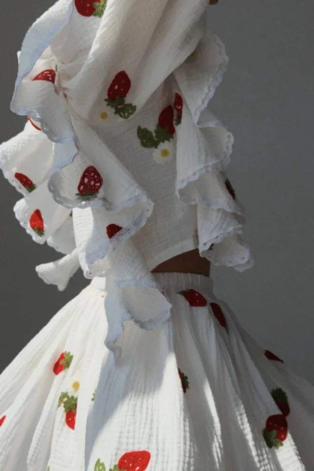 Detail shot of the ruffled sleeves and strawberry print on the white blouse and skirt.